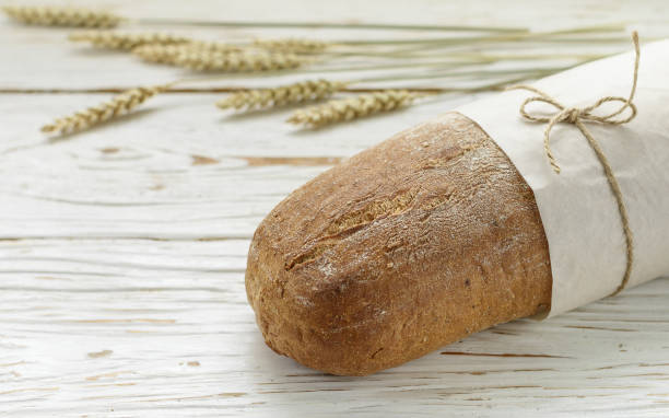 istock Loaf of fresh  bread and wheat ears on wooden table 968774600