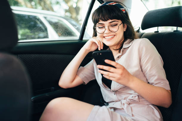 istock Beautiful young pretty girl is using a smart phone and smiling while sitting on back seat in the car 968782940