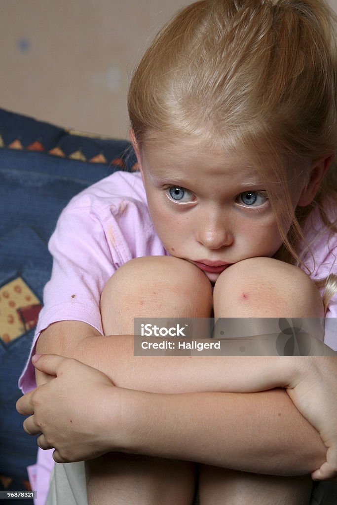 Young girl sitting with her knees pulled into her chest Little  girl looking at something frightening Girls Stock Photo