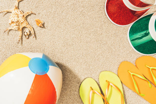 istock flat lay with colorful flip flops, beach ball, seashells and caps arranged on sand 968799884
