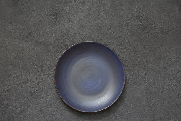 istock Blue round porcelain empty plate on a black stone background. Empty plate top view. 968819076