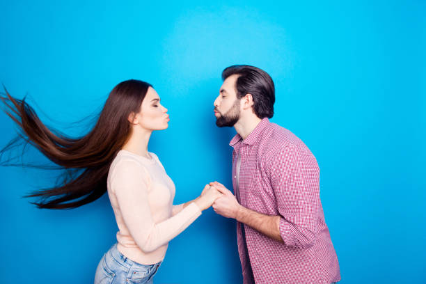 retrato de perfil de pareja moda elegante mantener ojos cerrados sosteniendo las manos de besos con faneca labios aislados sobre fondo azul. concepto de placer deseo deseo armonía - blowing men kissing blowing a kiss fotografías e imágenes de stock