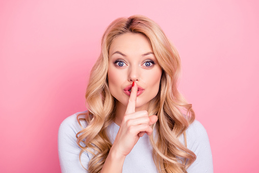 Shhh! Portrait of pretty mysterious girl in casual outfit showing silence sign holding forefinger on lips having curly hair modern hairdo isolated on pink background