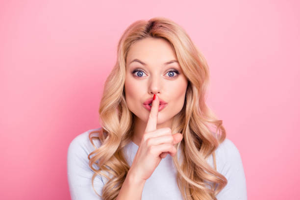 shhh! portrait of pretty mysterious girl in casual outfit showing silence sign holding forefinger on lips having curly hair modern hairdo isolated on pink background - finger on lips whispering secrecy silence imagens e fotografias de stock