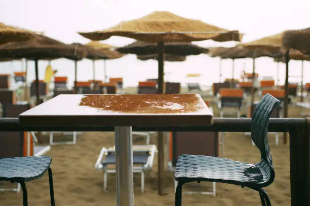 Sea shore cafe bar after summer rain. Wet table and chairs, beach umbrellas and sun loungers on the background. Film photo