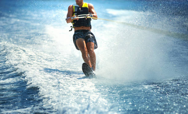 Wakeboarding. Closeup front view of an unrecognizable young man wakeboarding on a sunny summer day at open sea. He's wearing swimming suit and a life jacket. neoprene photos stock pictures, royalty-free photos & images