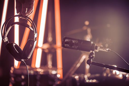 Studio microphone and headphones in the hand of a person close up, in a recording Studio or concert hall, with a drum set on the background in out-of-focus mode.