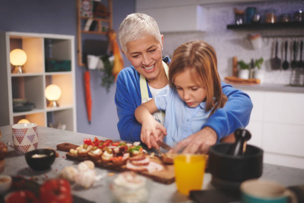 Active senior woman having fun time with her grandchild in the kitchen while preparing and tasting food.