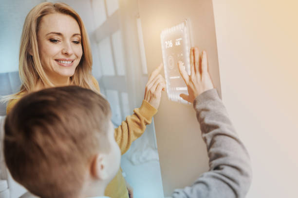 Kind mother looking at the son while using a modern device Unusual technology. Loving mother kindly looking at her curious son while using modern security system at home smart home family stock pictures, royalty-free photos & images