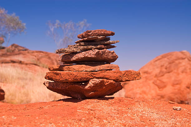 On the sandy surface, a tower is built from red and brown stones of various sizes and shapes, stacked on top of each other. The bottom stone is the largest, while the top one is the smallest.