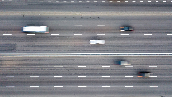 Aerial view shooting from drone on multi-lane highway in the evening, cars with headlights and parking lights included. Speedway, asphalt road, marking moving cars, blurred cars,