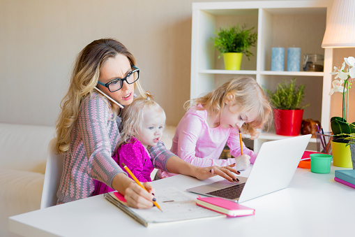 Busy woman trying to work with laptop while babysitting two kids