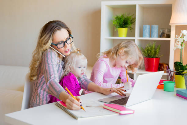 Busy woman trying to work while babysitting two kids Busy woman trying to work with laptop while babysitting two kids working hard stock pictures, royalty-free photos & images