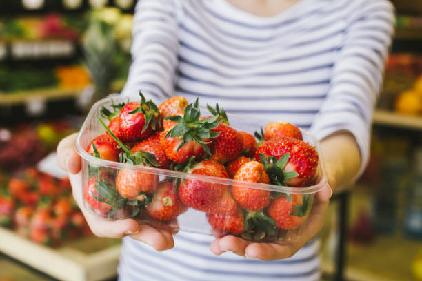 istock Beautiful young smiling woman holding a box with fresh strawberries and showing at the camera in a supermarket 968855708