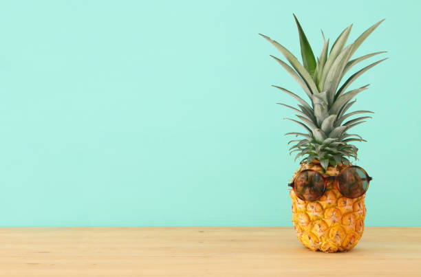 istock Pineapple on wooden table with funny sunglasses. Beach and tropical theme. 968856868