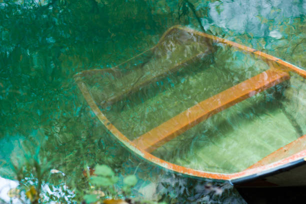 Wooden row boat sunken in green lake water.
