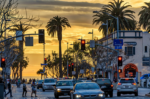 People and traffic on busy Santa Monica street with ocean sunset background.