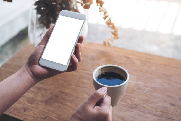 istock Mockup image of a woman's hand holding white mobile phone with blank desktop screen and coffee cup in cafe 968863314