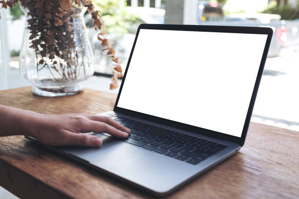 istock Mockup image of a hand using and touching laptop with blank white desktop screen on wooden table in cafe 968863992