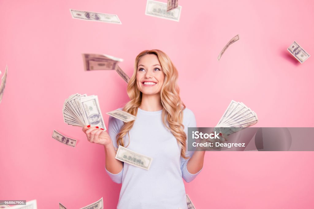 Portrait of pretty charming positive cute successful lucky cheerful girl standing under shower from money having a lot of money in hands isolated on pink background Currency Stock Photo