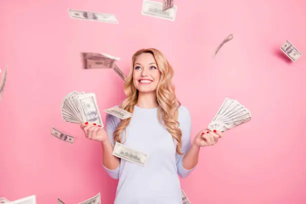 Photo of Portrait of pretty charming positive cute successful lucky cheerful girl standing under shower from money having a lot of money in hands isolated on pink background