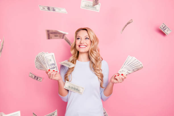 retrato de encantador positivo bonito bem sucedido alegre garota de sorte em pé sob o chuveiro de dinheiro tendo um monte de dinheiro em mãos isoladas em fundo rosa - holding money - fotografias e filmes do acervo