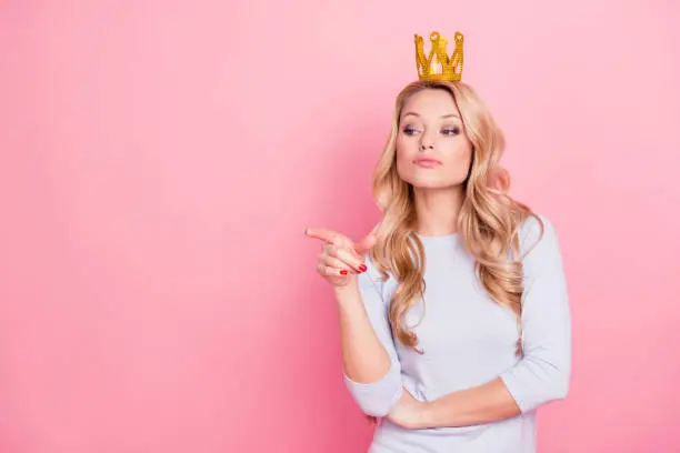 Portrait with copyspace empty place of confident proud arrogant woman with gold crown on her head pointing forefinger, miss I want, isolated on pink background