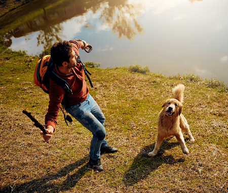 Full length shot of a handsome young man playing fetch with his dog by a lake in the park