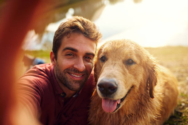 Smile, boy Cropped shot of a handsome young man and his dog taking selfies by a lake in the park selfie photos stock pictures, royalty-free photos & images