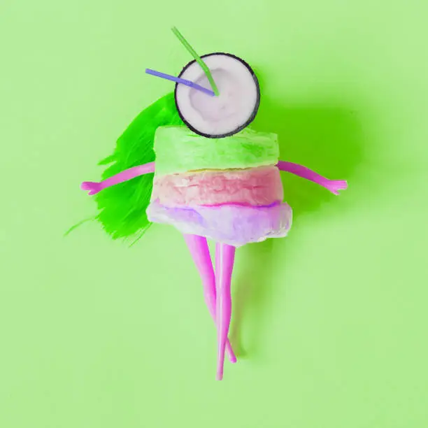 Photo of cocktail of half a coconut instead of a head of the purple doll dressed in cotton candy.