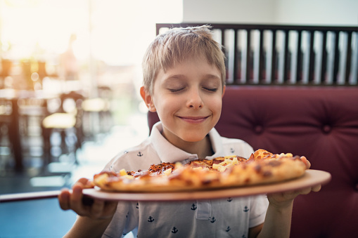 Little boy aged 8 smelling just cooked pizza in restaurant.
Nikon D850