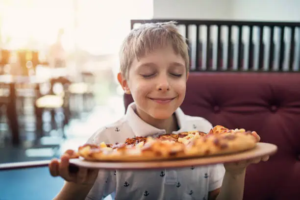 Photo of Little boy smelling pizza in restaurant