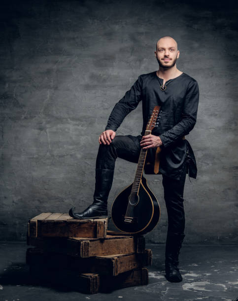 Image of male musicians in old traditional Celtic clothes holds vintage mandolin. Studio image of male musicians in old traditional Celtic clothes holds vintage mandolin. música stock pictures, royalty-free photos & images