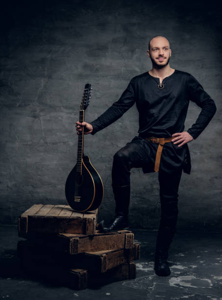 Image of male musicians in old traditional Celtic clothes holds vintage mandolin. Studio image of male musicians in old traditional Celtic clothes holds vintage mandolin. música stock pictures, royalty-free photos & images