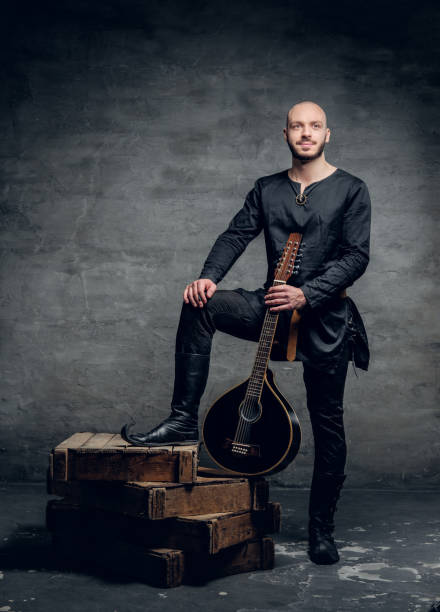 Image of male musicians in old traditional Celtic clothes holds vintage mandolin. Studio image of male musicians in old traditional Celtic clothes holds vintage mandolin. música stock pictures, royalty-free photos & images