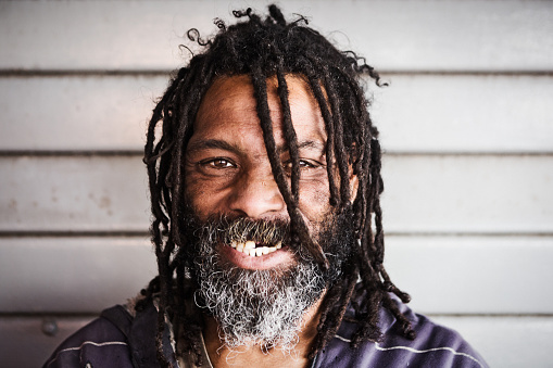 Homeless man with Rastafarian dreadlocks gives a happy,  gap-toothed smile.