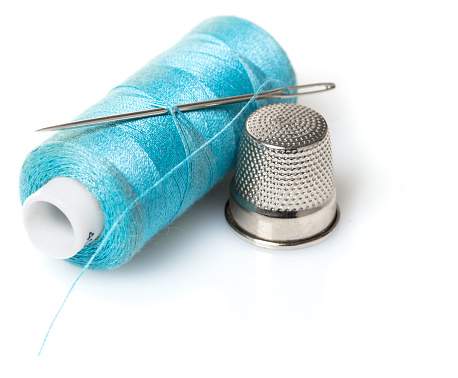 Thread with needle and thimble on white isolated background