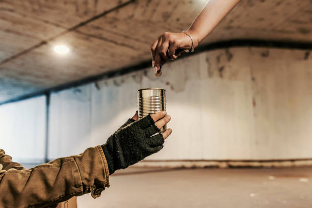 Can you help me please? Photo of a Unrecognizable Person, woman hand giving coin money to mature male beggar. He is sitting in the tunnel or subway station asking for money. Dirty hands of a Beggar receiving money from a kind female. begging currency beggar poverty stock pictures, royalty-free photos & images