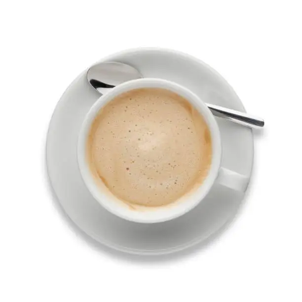 An aromatic cup of Cappuccino coffee, on a saucer, with a spoon, shot from above on white, with a drop shadow.