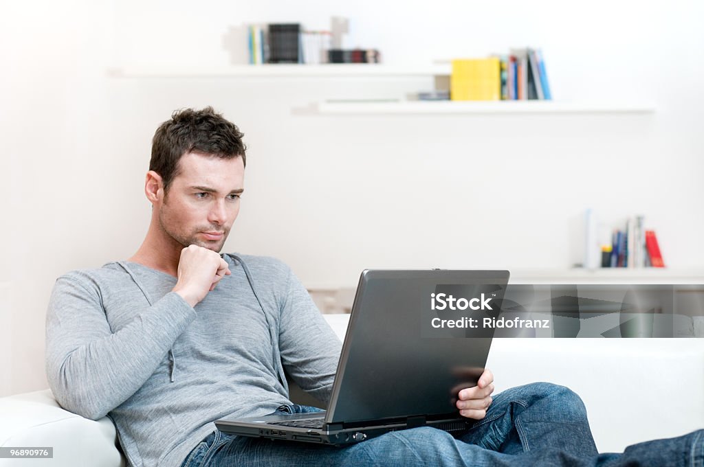 Man working on his laptop in a white living room Young man working absorbed on laptop at home copy space. Examining Stock Photo