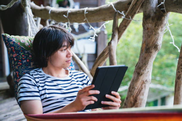 Young man lying in a hammock using a digital tablet computer Young man lying in a hammock using a digital tablet computer hammock men lying down digital tablet stock pictures, royalty-free photos & images