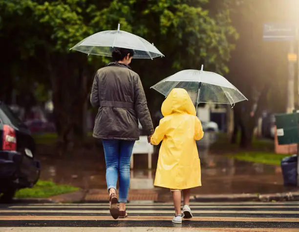 Rearview shot of an unrecognizable little boy and his mother holding hands and walking in the rain outside