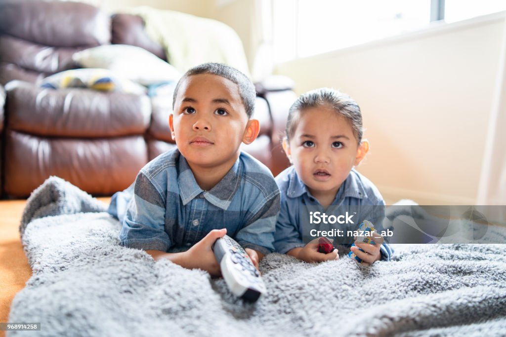 Two brothers lying down and watching TV. Maori kids watching TV in Auckland, New Zealand. Watching TV Stock Photo