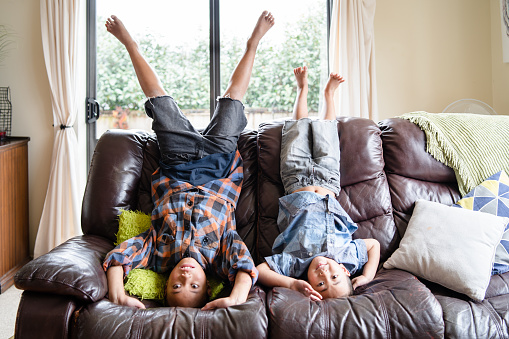 Maori Kids at home having fun being upside down on sofa in living room Auckland, New Zealand.