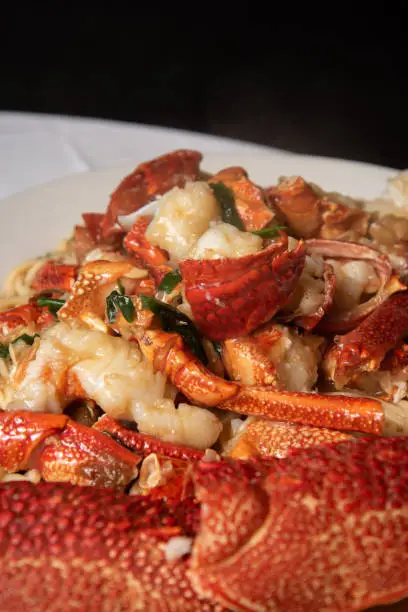 Photo of Stir-fried lobster with ginger and green onions on top of a bed of noodles