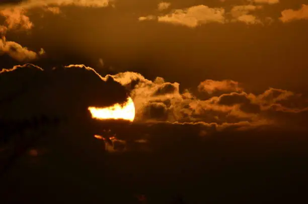 A long distance shot of the sun beginning to set. Everyone with a telephoto lens has one of these. This is mine. The sun behind the clouds.
