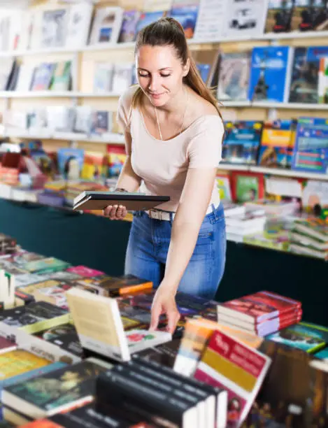 Portrait of smiling young woman picking textbooks in book store