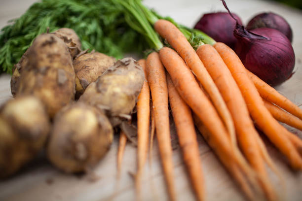 Close up color image depicting a bowl of chopped vegetables, namely carrots and parsnips and fresh parsley, with a background of fresh fruit - grapes, oranges and bananas. The fruit is blurred out of focus, providing room for copy space.