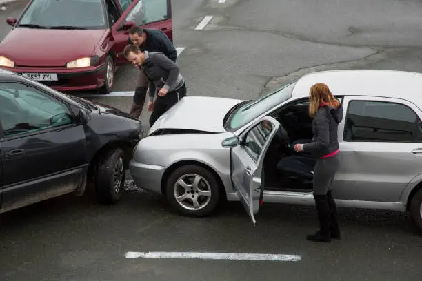 Two men looking at cars collision on road, woman standing near car.