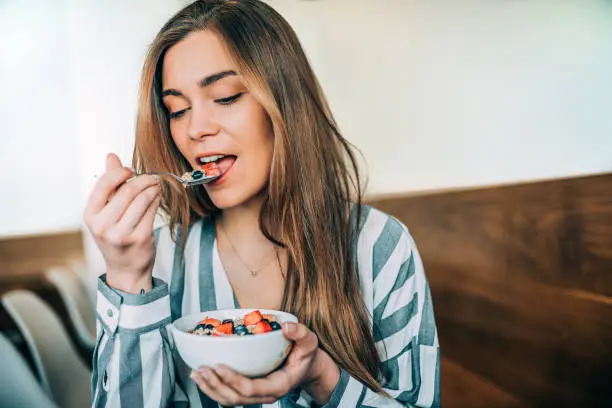 Photo of woman close up eating oat and fruits bowl for breakfast